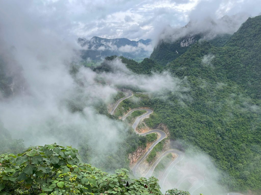 Winding mountain road through mist-covered green karst mountains in Cao Bang, northern Vietnam.